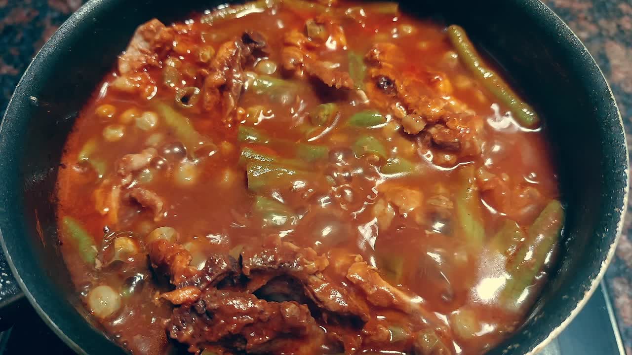 A pot filled with simmering hearty stew containing green beans and meat in tomato sauce, home cooking
