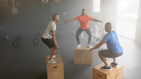 diverse male group fitness class jumping onto boxes, cross training at gym, in slow motion