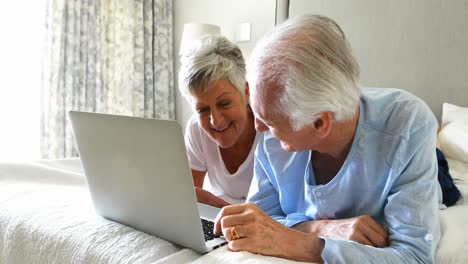 smiling senior couple using laptop on bed in bedroom