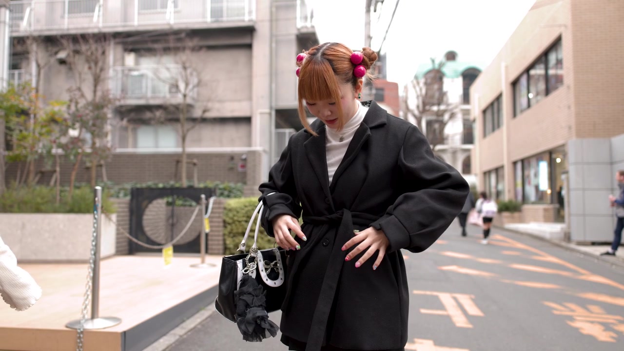 Tokyo'da bir sokakta duran genç bir Asyalı kadın, siyah kabanının kemerini bağlıyor.