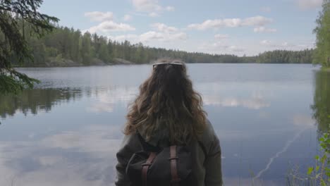 Joven-Mochilero-Caucásico-Cautivado-Por-Un-Idílico-Lago-Con-Un-Denso-Bosque-En-Finlandia