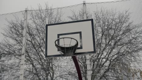 a detailed slow motion arc shot of a basketball hoop with a protective net, set against winter trees and urban surroundings