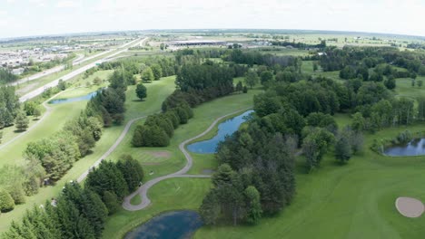 Wide-aerial-view-of-golf-course,-tree-lined-fairways,-sand-trap,-water-hazard,-greens-and-cart-path