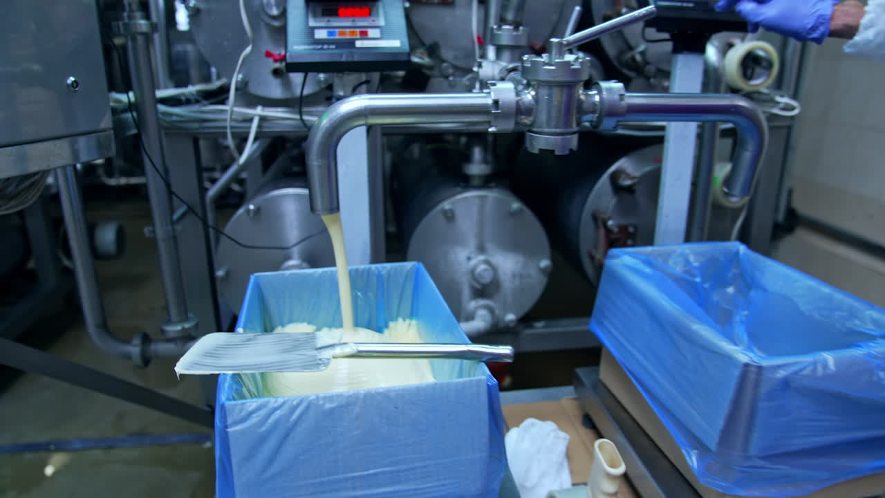 Industrial equipment for milk production. Fresh milk product pouring into special containers. Making butter on a milk factory.