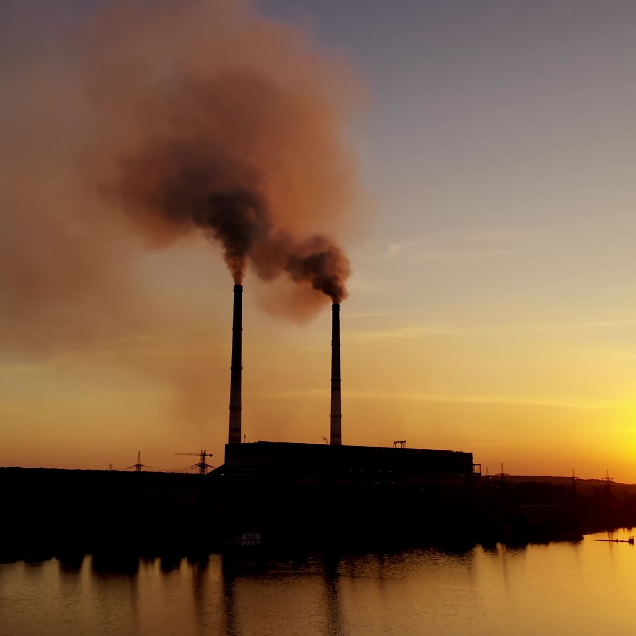 Industrial factory near the river at sunset. Smoke comes out of the pipes of a huge plant in the evening. Environmental pollution.