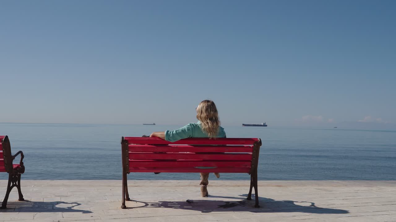 Young confident business woman sitting on red bench and looking at endless ocean
