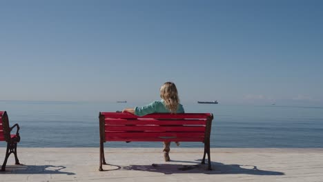 young confident business woman sitting on red bench and looking at endless ocean