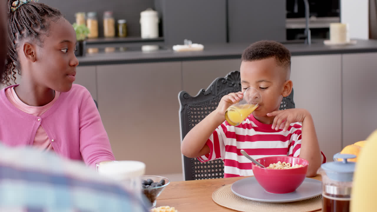 African american brother and sister eating breakfast at table in kitchen, slow motion