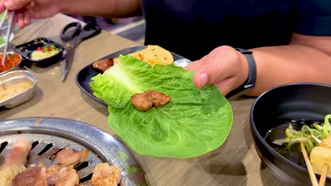 hands prepare a korean bbq lettuce wrap with grilled meat and vegetables in a vibrant bangkok setting