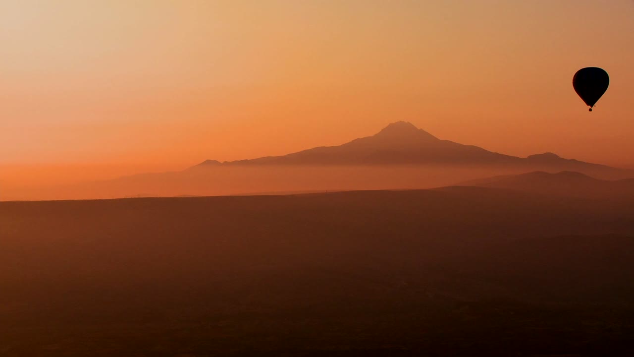 magnífica toma aérea de un globo aerostático recortado contra montañas distantes en capadocia, turquía 1