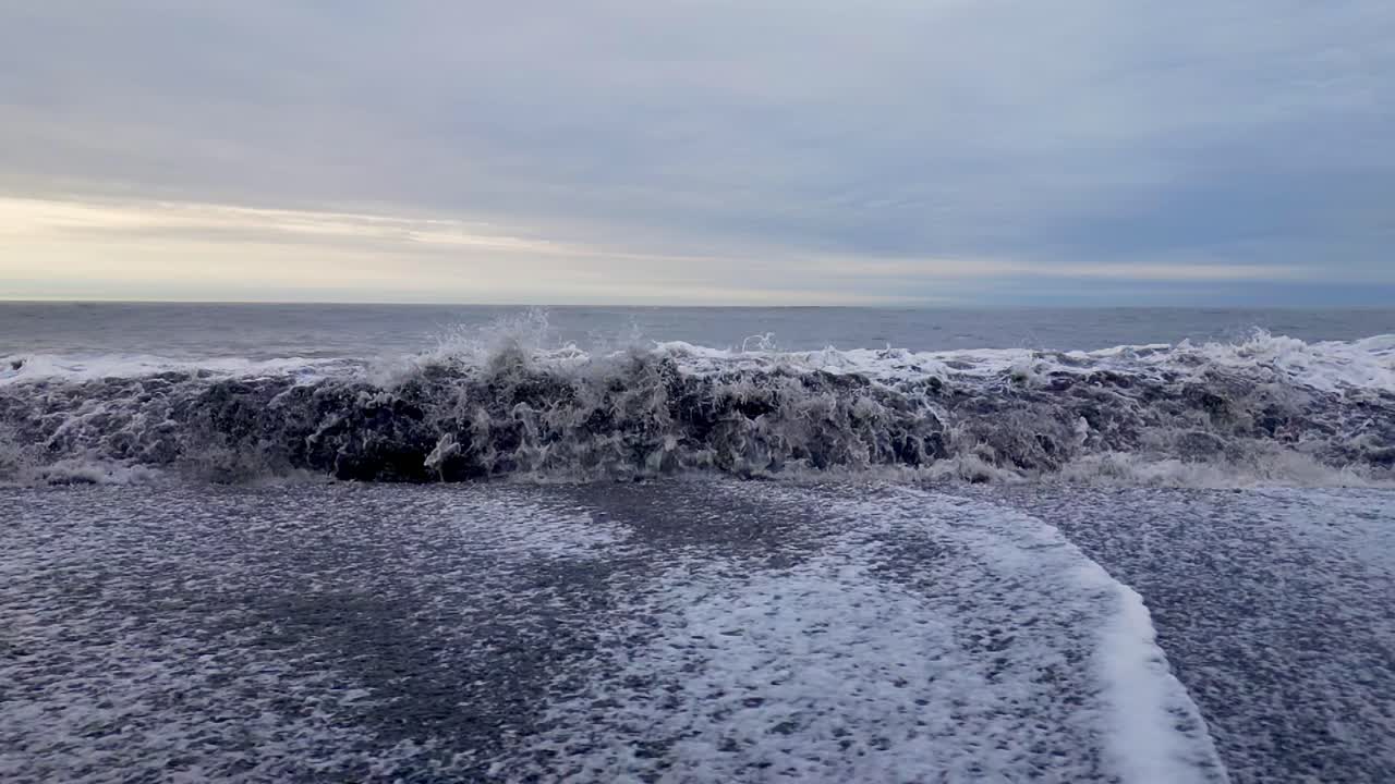 검은 모래 해변에 부서지는 하얀 거품을 형성하는 서핑 파도