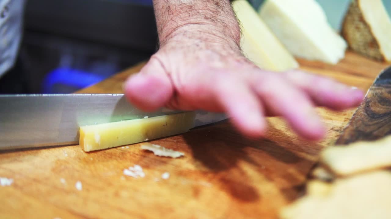foto de una persona cortando queso con un cuchillo en una tabla de madera a cámara lenta