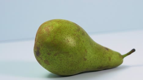 fresh big green pear rotates slowly on a light blue background, healthy food concept, close up shot, camera rotate left