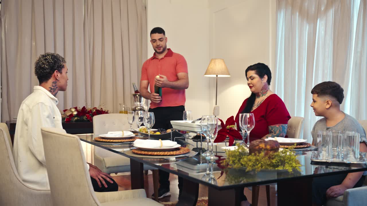 A group of people gathered around a dining table, with a man pouring wine for the guests