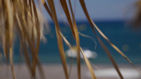 Handheld-Closer-Close-Up-of-Dry-Palm-Leaves-Moving-by-The-Wind-from-a-Tiki-Hut-Umbrella-on-The-Black-Lava-Beach-in-Perissa-Santorini-in-Greece-Europe