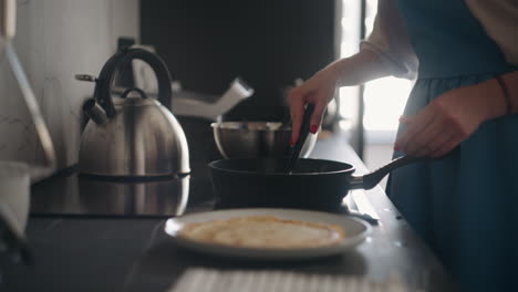 una mujer está cocinando el desayuno para la familia el domingo por la mañana. una ama de casa con un delantal azul está fritando panqueques.