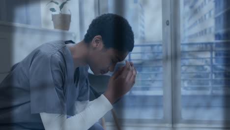 animation of rain on window over unhappy african american female doctor holding head in hands