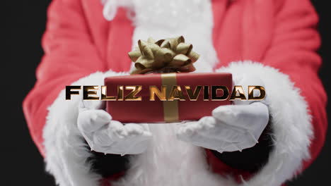 feliz navidad texto en oro sobre la sección media de padre navidad agarrando regalo