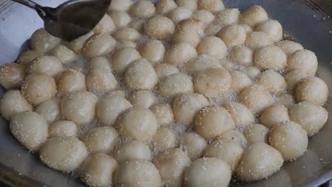 vendedor ambulante de comida friendo bolas de semillas de sésamo, un tipo de pastel chino hecho de harina de arroz glutinoso con relleno de pasta de judías verdes y cubierto con semillas de sésamo blancas en aceite caliente en una sartén grande