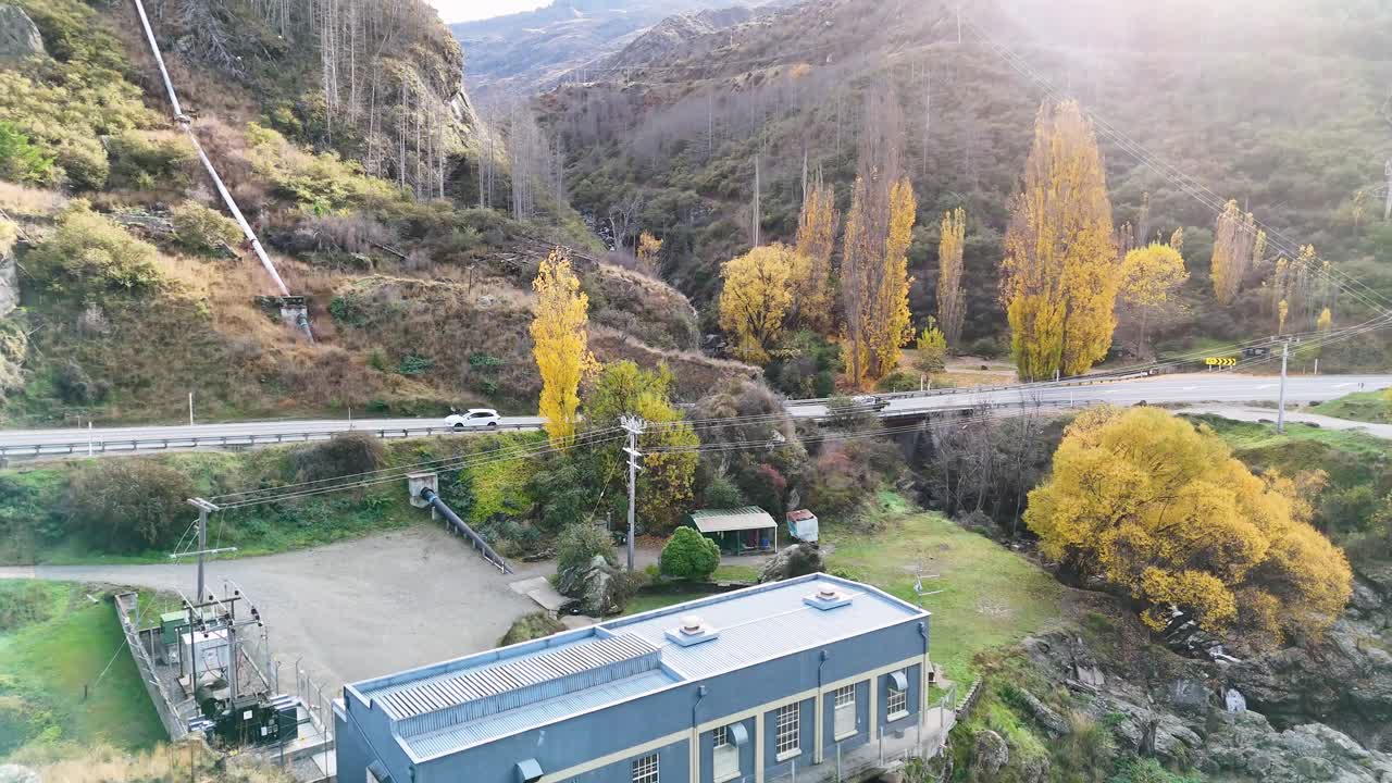 Drone footage captures a hydroelectric power station amidst autumn foliage in Queenstown, New Zealand, with dynamic camera movement and natural lighting