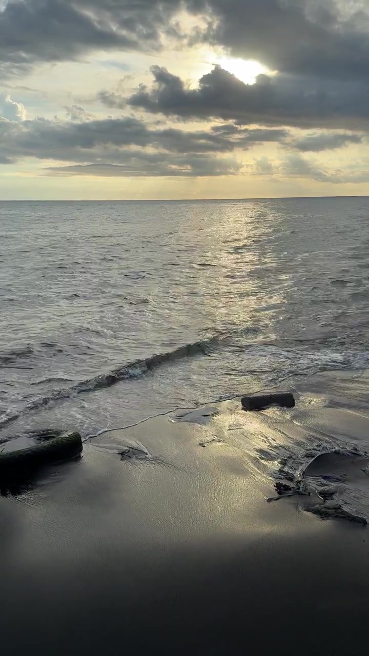 Riflesso dorato del tramonto sulle onde dell'oceano e sulla spiaggia di sabbia scura.