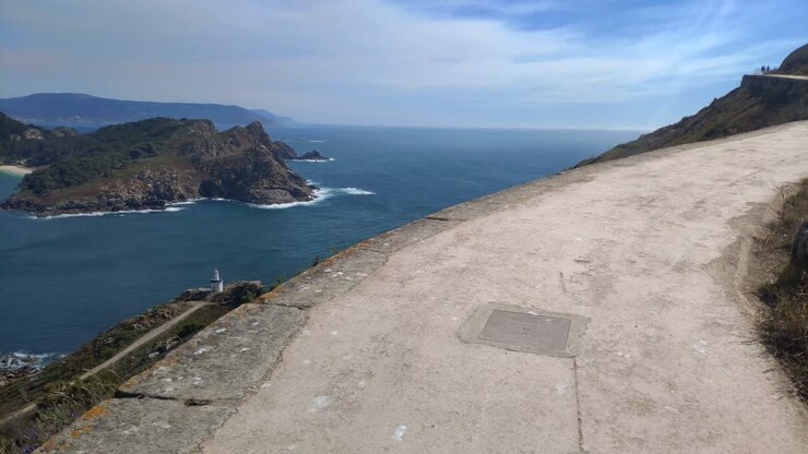 Persone che camminano su un sentiero di montagna con punto panoramico in vetta e l'isola sullo sfondo nel mare, giornata di sole, ripresa in movimento in avanti con rotazione a destra, Isola di Cíes, Galizia, Spagna