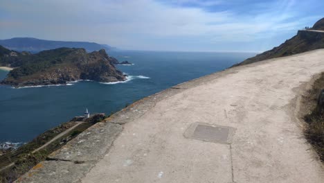 people climbing on the mountain path with viewpoint at the summit and the island in the background in the sea, sunny day, shooting traveling forward rolling to the right, cíes island, galicia, spain