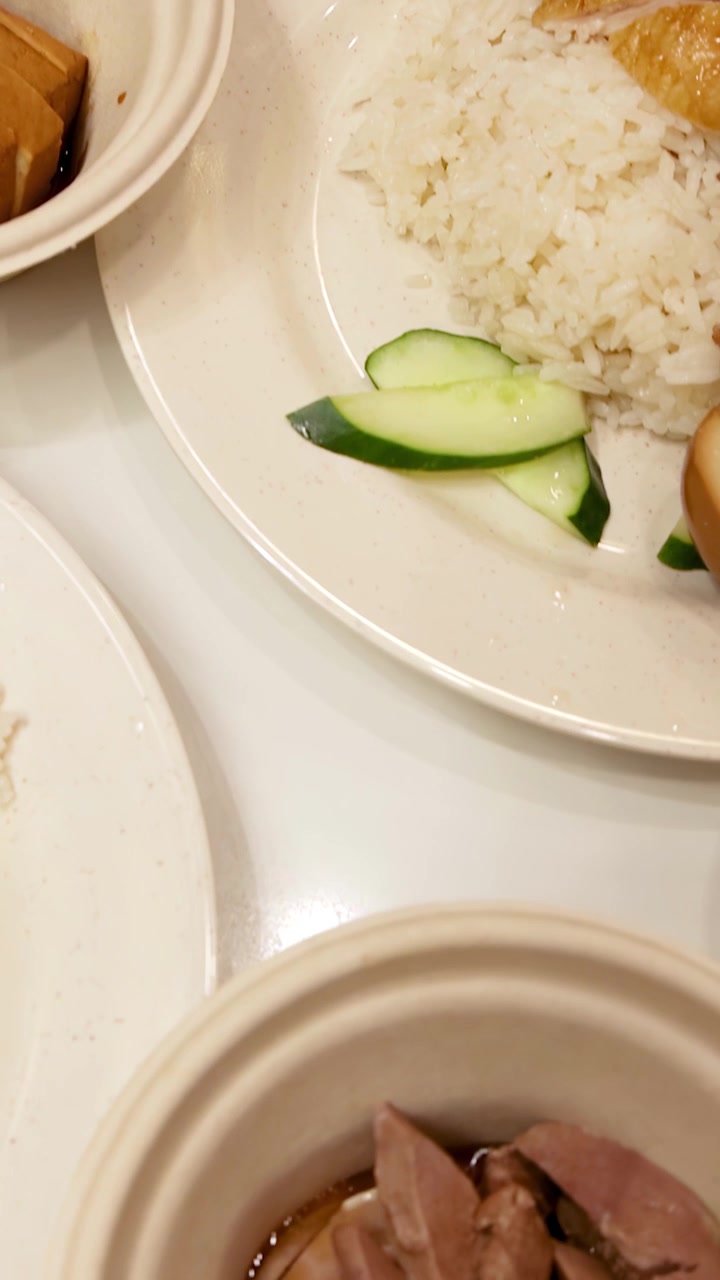 Close-up of Hainanese chicken rice plates with roasted, steamed chicken, rice, cucumber, and egg.