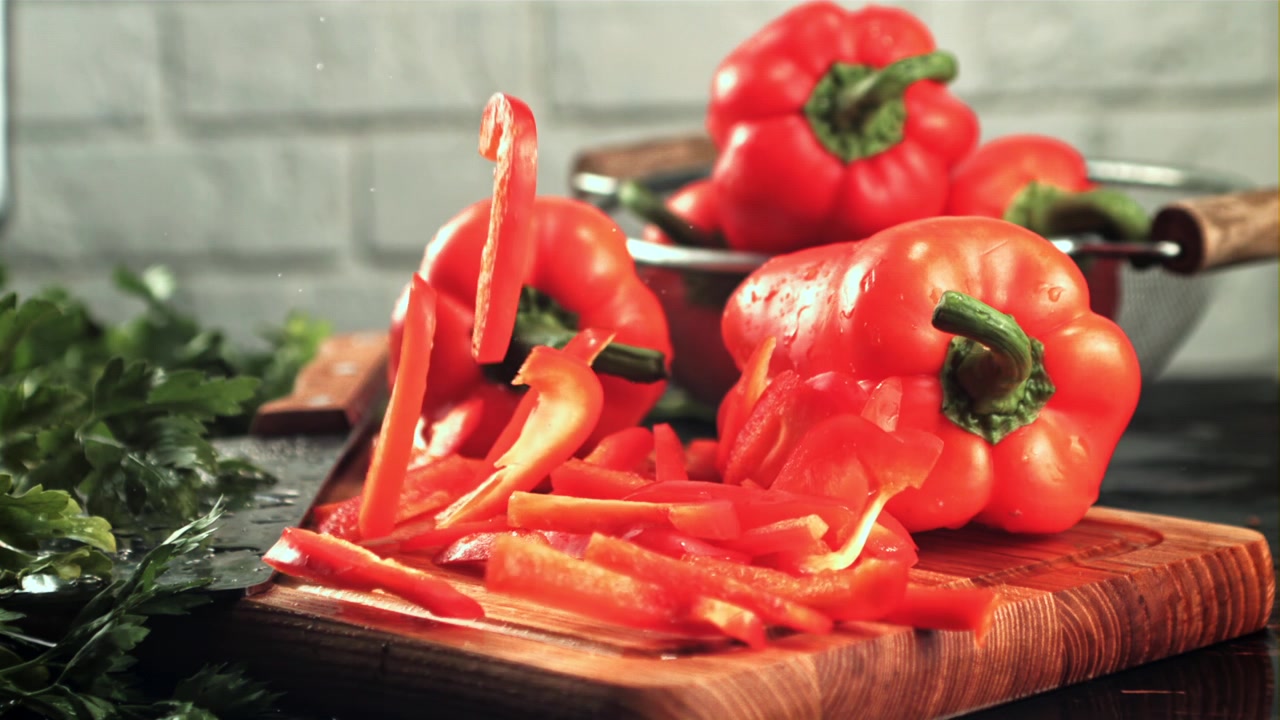 Nakrájená červená paprika padající na dřevěné prkénko.