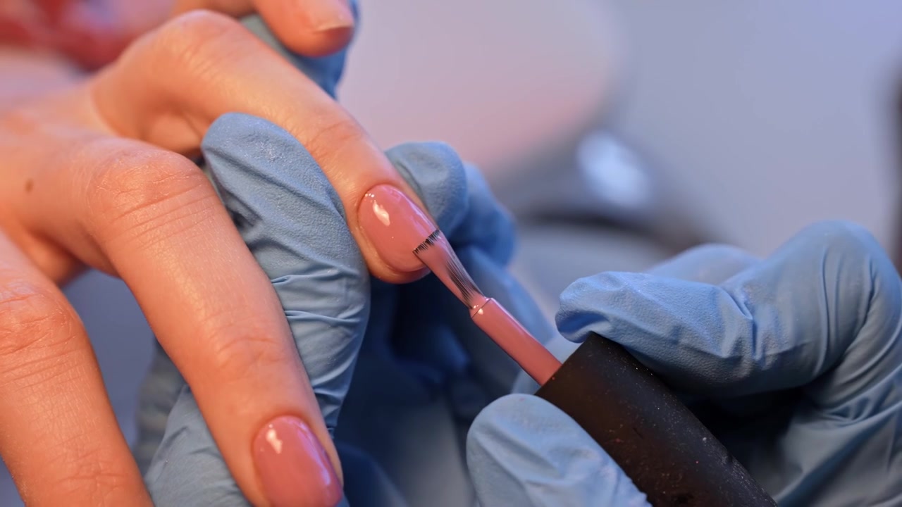 Close-up of a nail technician applying nude gel polish to a client’s fingernail during a professional manicure session in a beauty salon.