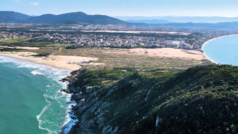 escena de drones aéreos de playa paradisíaca urbanizada con dunas de arena, montañas y playa de mar de santinho florianópolis cima de la montaña y ciudad en el horizonte