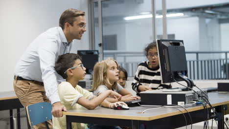 Multiethnic-children-doing-task-during-computer-science-lesson-while-teacher-watching-them