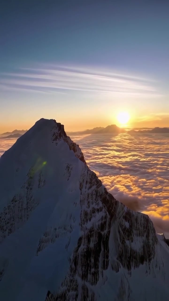 Aerial View of Snow-Covered Mountain Peak Above Clouds at Sunset