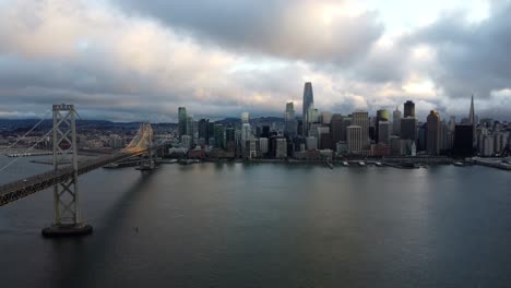 4k 30fps aerial drone footage of san francisco city skyline and the oakland bay bridge - cars travel along the highway, stormy cumulus clouds, calm bay water, sunset reflecting off waves, landscape