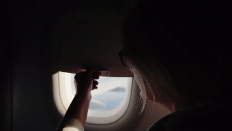 a woman opens the porthole curtain and looks out the window of the plane