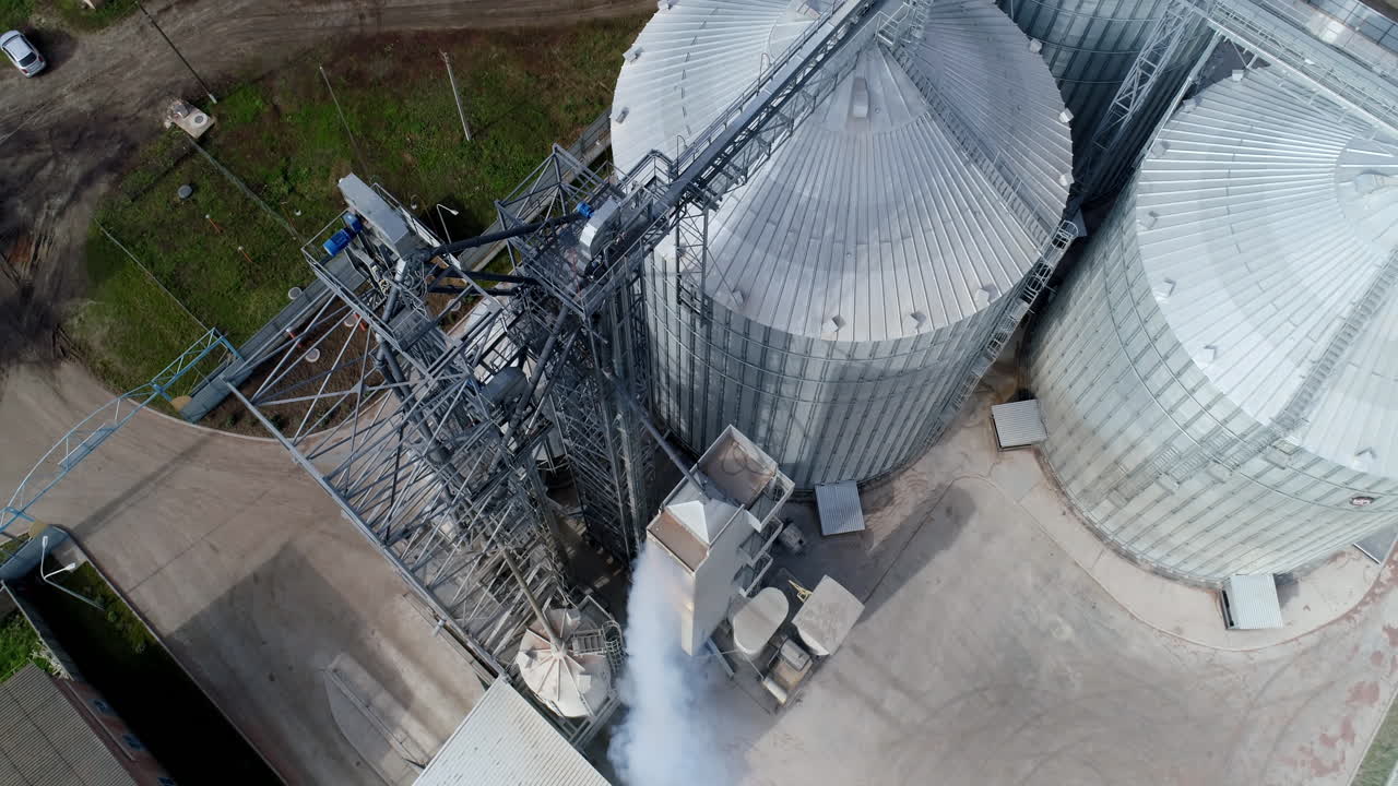 Industrial elevators from above. Metal construction of granary. Smoke from manufacturing rising up. Top aerial view.