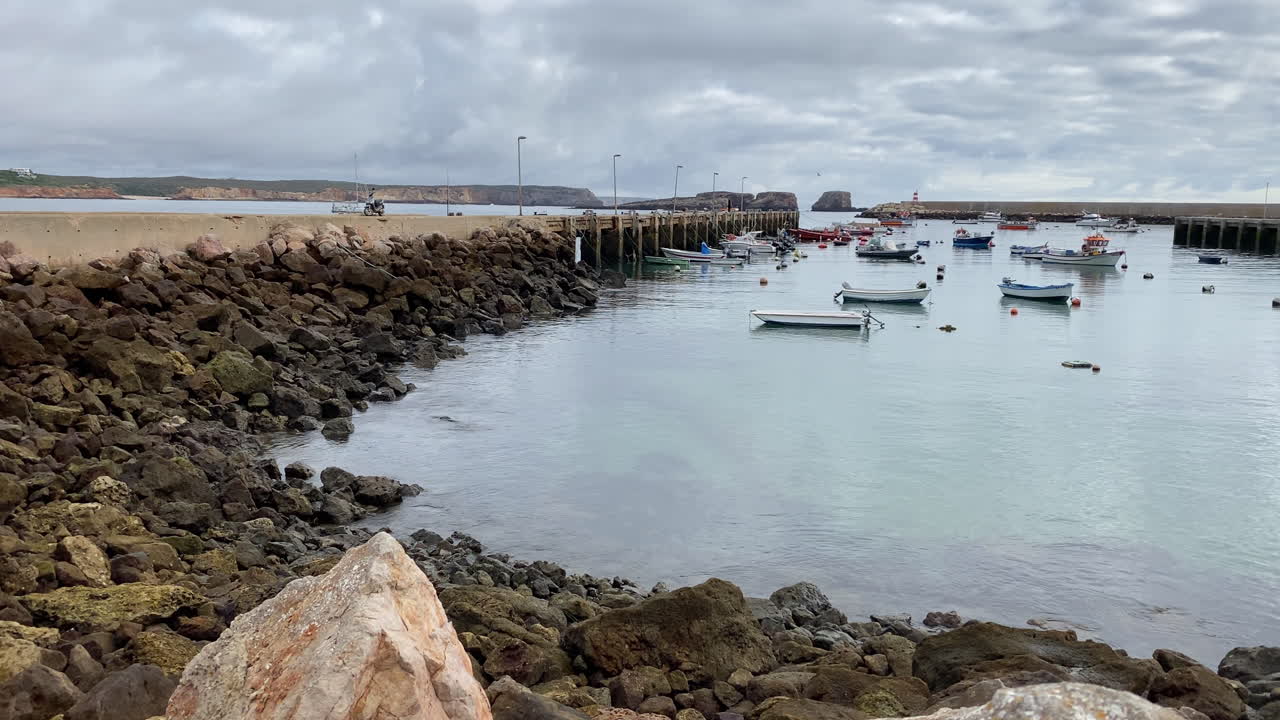 wide View of Sagres harbor framed by rocks and distant cliffs under a moody Atlantic sky