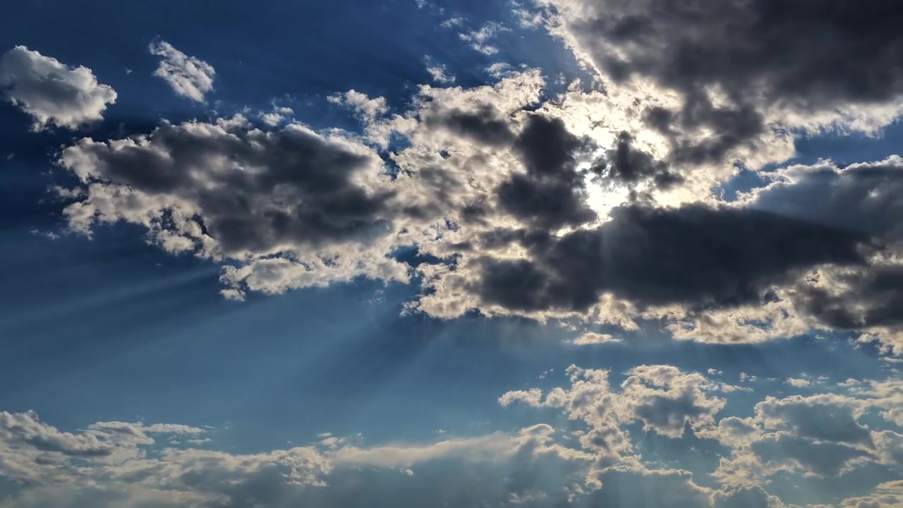 Timelapse 4K con drone di un sistema meteorologico dinamico. Raggi di sole spettacolari e fasci di luce radiosi penetrano attraverso nuvole scure e in rapido movimento contro un cielo azzurro brillante in questa atmosfera drammatica