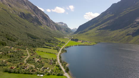 Vista-De-Un-Pequeño-Pueblo-Y-Carretera-Al-Pie-De-Exuberantes-Montañas-Junto-Al-Lago-Eidsvatnet-Cerca-De-Geiranger,-Noruega