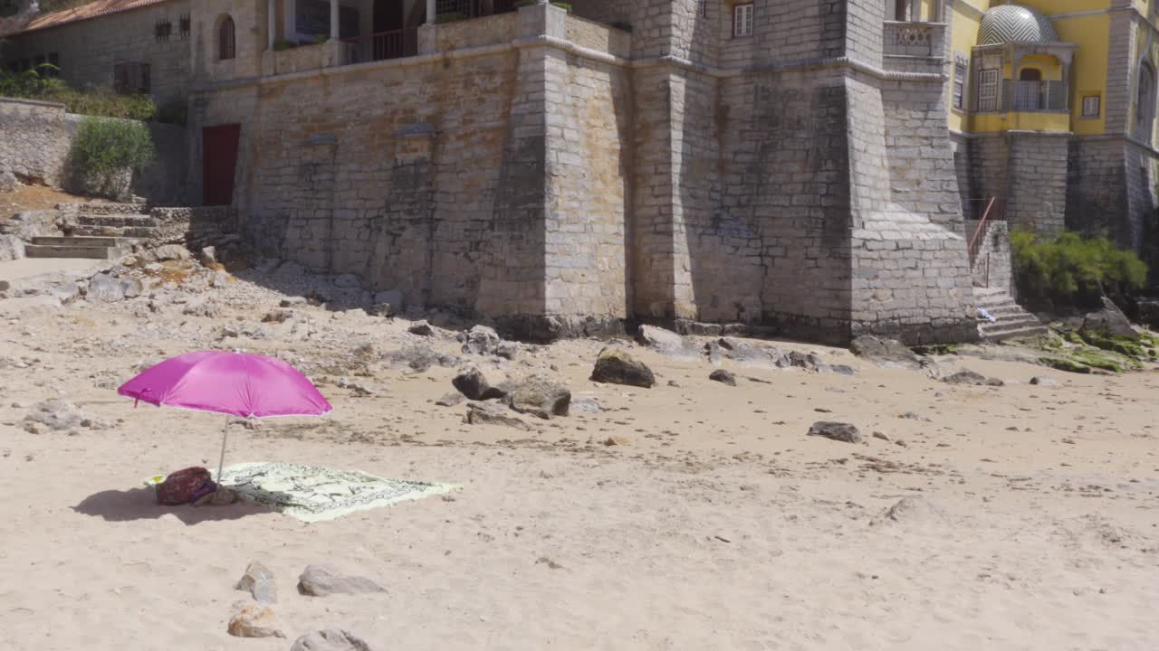 Una playa vacía en marea baja con una sombrilla junto al Museo Condes de Castro Guimarães en Cascais, Portugal