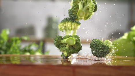 slow motion of fresh green broccoli slices falling on wet wooden board in a kitchen