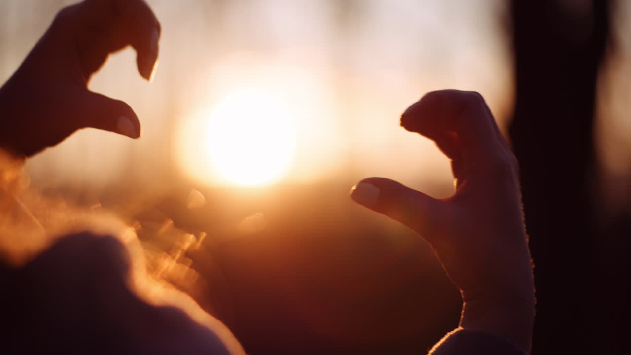 여자는 태양에 대 한 심장 모양의 손을 확인