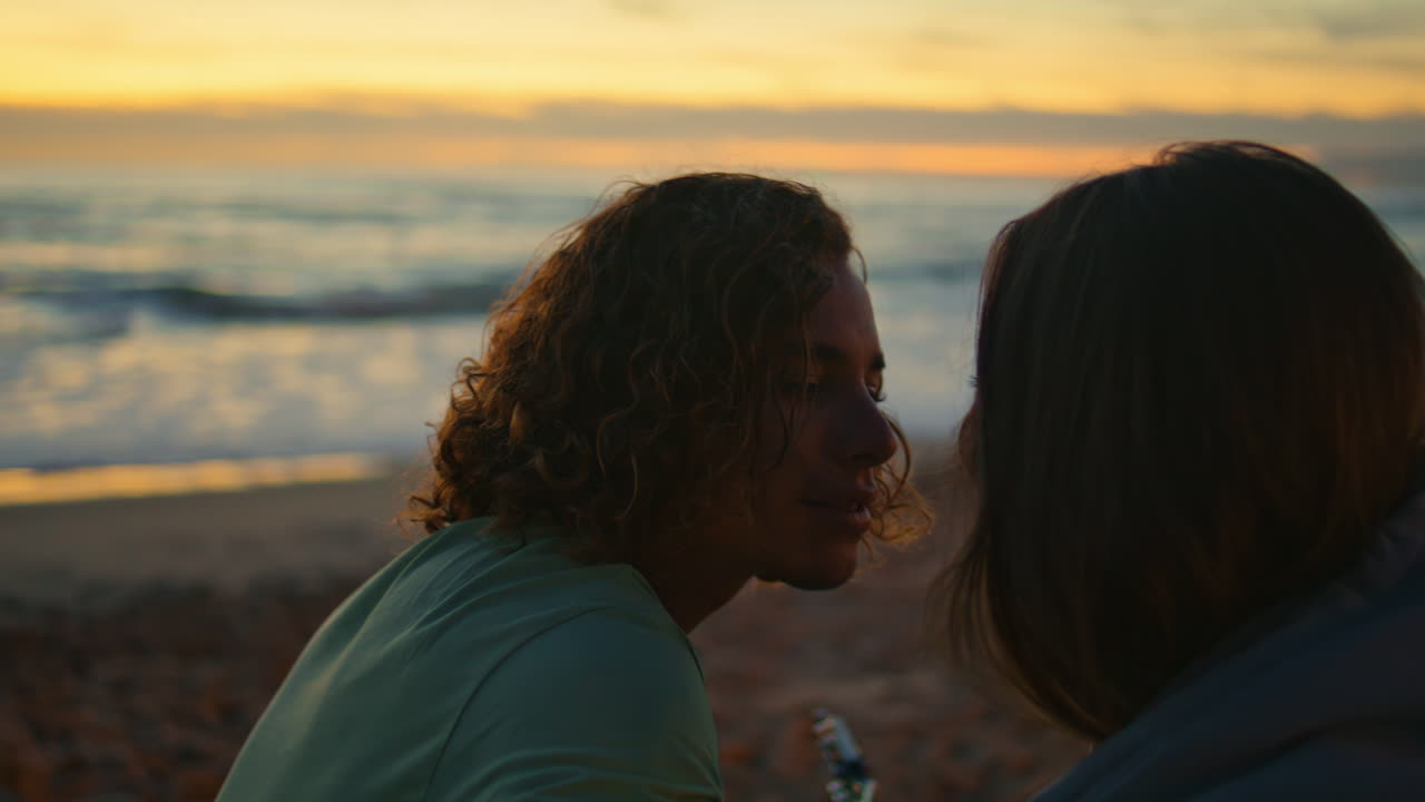 Ragazzo musicista che bacia la fidanzata al tramonto nella natura, primo piano. Uomo che suona la chitarra.