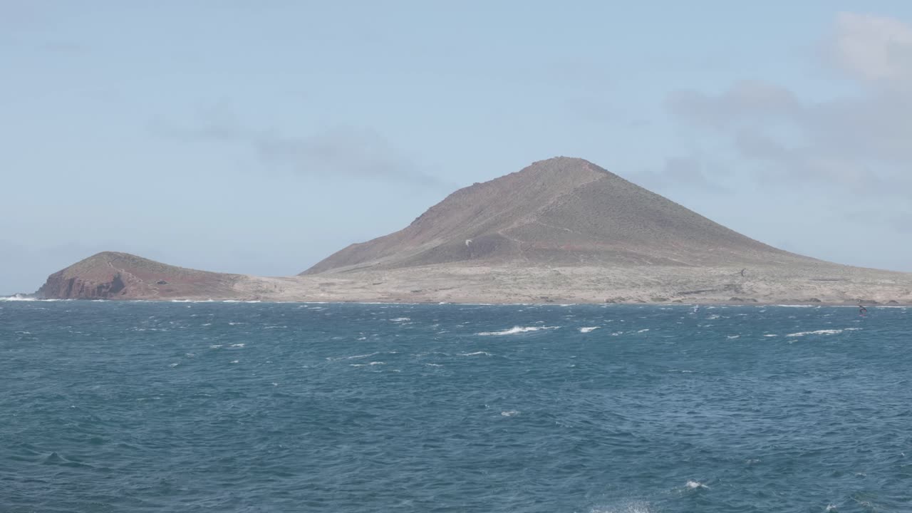 A volcanic hill by the ocean and the ocean on a sunny day in Montana Roja, El Médano, Tenerife, Canary Islands, Spain.
