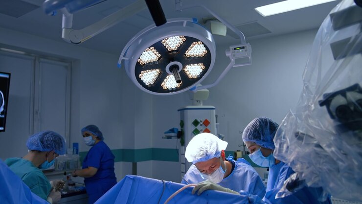 Two doctors bent above the patient performing operation. Male assistant using scissors preparing materials for the neurosurgeon.