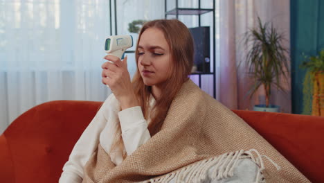 sick ill girl suffering from cold or allergy measures the temperature with an electronic thermometer