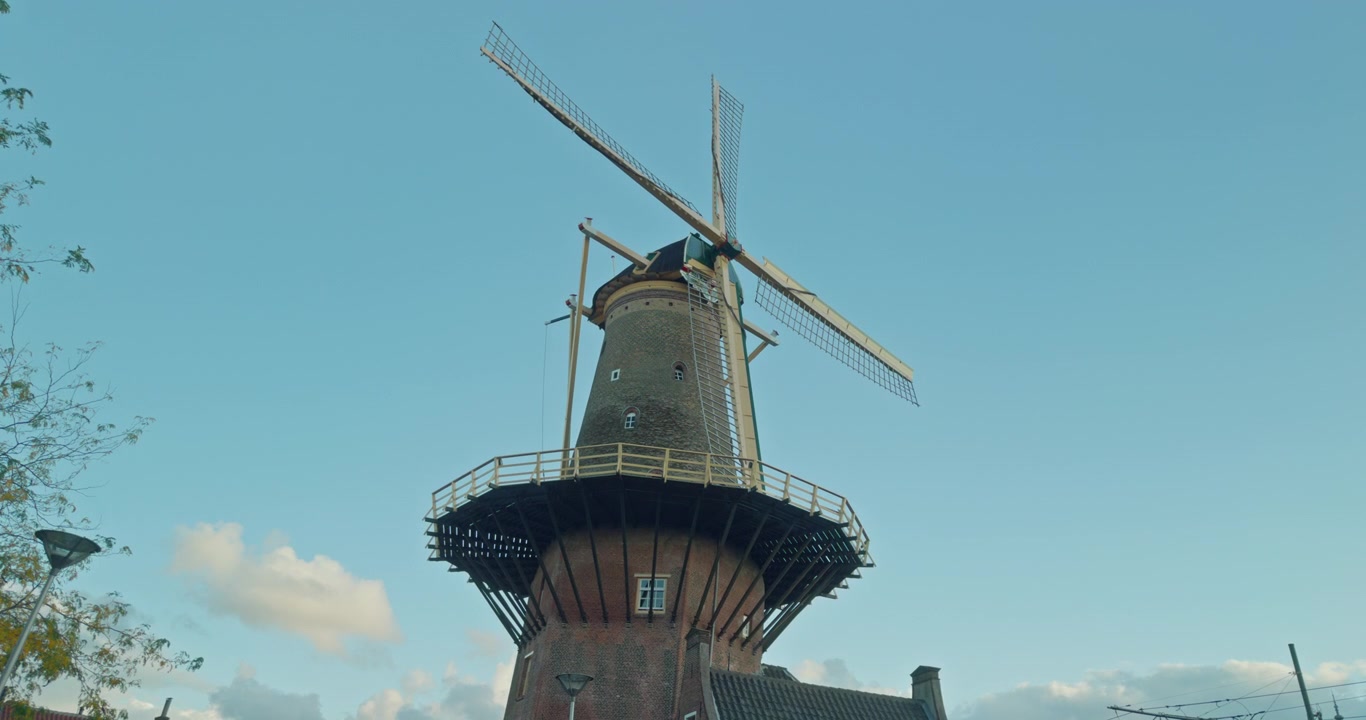 Struttura tradizionale di mulino a vento olandese a Delft, Paesi Bassi, Europa, con sfondo di cielo azzurro limpido e nuvole, pale in legno, torre in mattoni e vista sul paesaggio urbano circostante