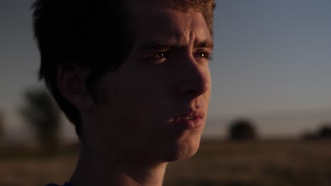 primer plano de un joven adolescente de pie en un campo viendo la puesta de sol