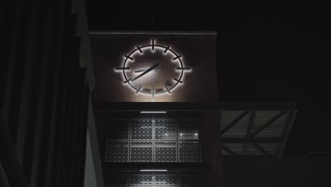 large glowing analog clock on side of downtown brick building