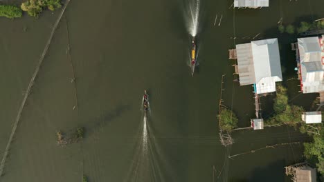 top down aerial of long boat traveling through floating village at inle lake